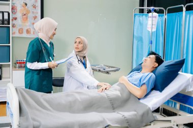 Hastane koğuşundaki bir hastaya bakım sunan tesettürlü doktorlar takım çalışması, profesyonellik ve şefkatli bir sağlık ortamı sunuyorlar..