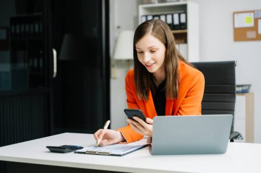 Ofiste çalışırken dizüstü bilgisayar ve akıllı telefon kullanan kadın girişimci 