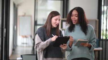 Ofiste yeni bir proje üzerinde çalışan mutlu iş kadınları dijital tablet kullanıyorlar ve not defterine not tutuyorlar. 