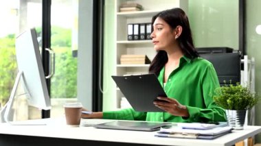 gülümseyen Asyalı iş kadını iş yerinde bilgisayar kullanıyor ve panoyu tutuyor. 