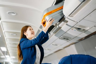 Çekici Asyalı bayan yolcu bavulu uçağın tepesindeki kutuya koyuyor.