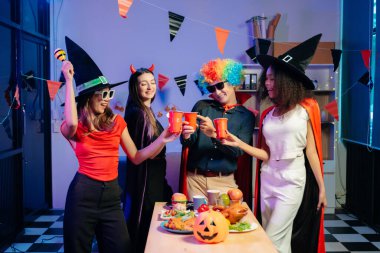 Kostümlü iş arkadaşlarıyla neşeli bir ofis Cadılar Bayramı partisi, içkilerle kutlama ve takım çalışmasını teşvik ve şenlik ruhu.