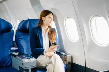 Başarılı bir Asyalı iş kadınının portresi. Uçakta birinci sınıfta oturuyor ve sıcak kahvenin tadını çıkarıyor. 