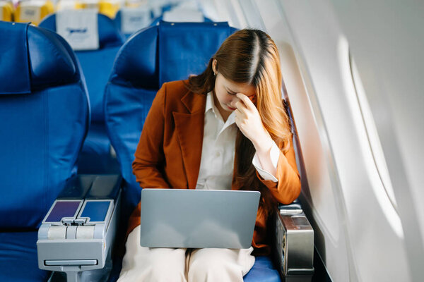 Фото расстроенной женщины, сидящей в кресле самолета у нее болит голова и с помощью ноутбука 