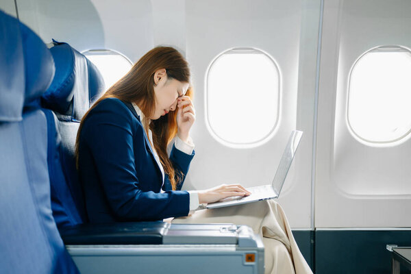 Фото расстроенной женщины, сидящей в кресле самолета у нее болит голова и с помощью ноутбука 