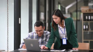 Asyalı işadamı sunar ve meslektaşına dizüstü bilgisayar kullanarak yeni projeyi açıklar. Modern ofis odasında çalışırken takım çalışması, finansal pazarlama ekibi..