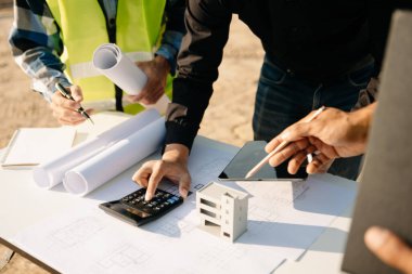 İnşaat endüstrisindeki bir inşaat sahasında mimarlık ekibi taslak üzerinde çalışıyor ve dijital tablet kullanıyor. 