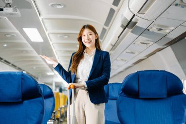 Çekici Asyalı kadın yolcu bavuluyla uçakta duruyor ve el kol hareketi yapıyor. 