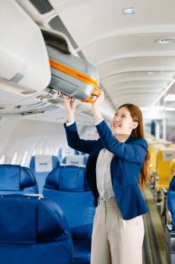 Çekici Asyalı bayan yolcu bavulu uçağın tepesindeki kutuya koyuyor.
