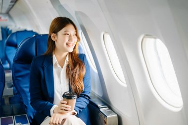 Başarılı bir Asyalı iş kadınının portresi. Uçakta birinci sınıfta oturuyor ve sıcak kahvenin tadını çıkarıyor. Pencereden dışarı bakıyor. 