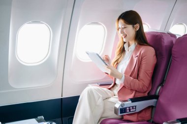 Genç Asyalı iş kadını dijital tabletle uçakta birinci sınıfta.  