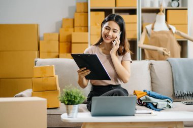 Genç işletme sahibi akıllı telefondan konuşuyor ve online siparişleri kontrol ediyor.