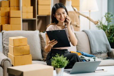Genç işletme sahibi akıllı telefondan konuşuyor ve online siparişleri kontrol ediyor.