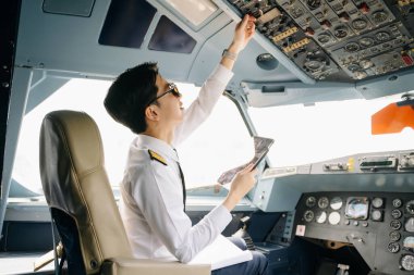 Asyalı kendinden emin üniformalı erkek pilot kalkış sırasında uçak kokpitinin içinde oturuyor.
