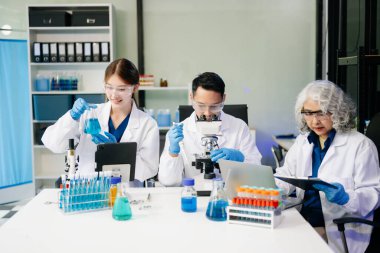 Bilim adamlarından oluşan bir ekibin laboratuvar ekipmanları, dizüstü bilgisayar ve dijital tabletlerle araştırma, test ve yenilikler üzerinde işbirliği yaptığı dinamik bilim laboratuvarı.