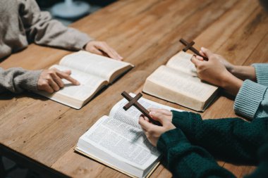 Group of Christians sit together and pray around a wooden table with blurred Bibles in homeroom. Prayer for brothers, faith, hope, and seek the blessings of God. clipart