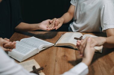 Bir grup Hıristiyan birlikte oturup ahşap bir masanın etrafında otururlar ve sınıfta bulanık incillerle dua ederler. Allah 'ın lütuf ve ihsanını dileyin..