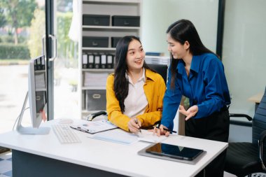 İki gülümseyen Asyalı iş kadını modern ofiste çalışır ve iş planlarını tartışırlar..