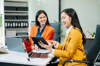 İki Asyalı iş kadını tablet ve dizüstü bilgisayar kullanarak modern ofiste çalışıp iş planlarını tartışıyor. 