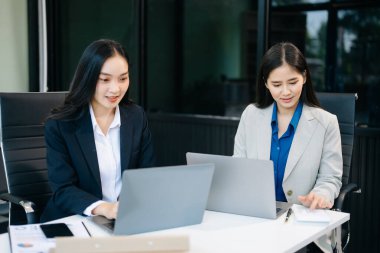 İki Asyalı iş kadını bilgisayar kullanarak modern ofiste iş planlarını tartışıyor. 