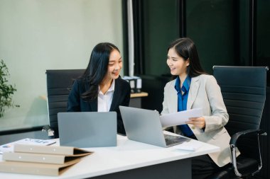İki Asyalı iş kadını bilgisayar kullanarak modern ofiste iş planlarını tartışıyor. 