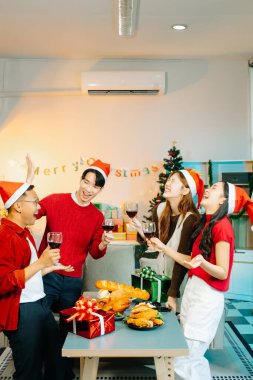 Bir grup Asyalı genç arkadaş birlikte Noel partisinde eğleniyor, şarap içiyor, yemek yiyor, evde kutluyorlar.