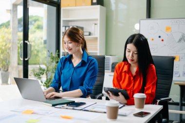 Asyalı iş arkadaşları dizüstü bilgisayar ve dijital tablet kullanıyorlar. Modern ofiste çalışan finansal pazarlama ekibi. 