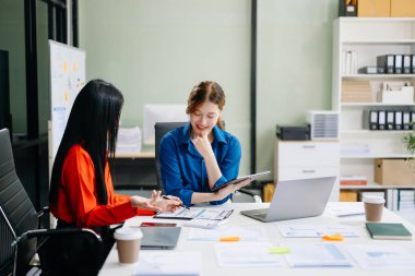 Asyalı iş arkadaşları dizüstü bilgisayar ve dijital tablet kullanıyorlar. Modern ofiste çalışan finansal pazarlama ekibi.  