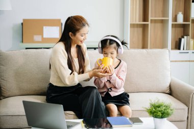 Neşeli anne ve kız kanepede güzel vakit geçiriyorlar, gülümsüyorlar ve birlikte çay içiyorlar. Aile teması için mükemmel.