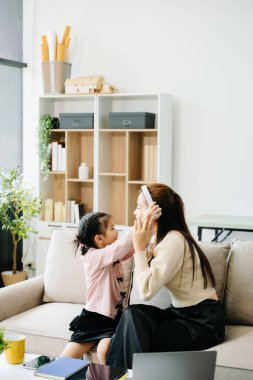 Neşeli anne ve kız kanepede kaliteli zaman geçiriyorlar, birlikte kulaklıklarda gülüyorlar ve müzik dinliyorlar. Aile teması için mükemmel.