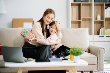 Neşeli anne ve kız kanepede güzel vakit geçiriyorlar, gülümsüyorlar ve sarılıyorlar. Aile teması için mükemmel.