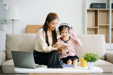 Neşeli anne ve kız kanepede güzel vakit geçiriyorlar, gülümsüyorlar ve akıllı telefon kullanıyorlar. Aile teması için mükemmel.