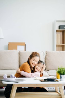 Neşeli anne ve kız kanepede güzel vakit geçiriyorlar, gülümsüyorlar ve sarılıyorlar. Aile teması için mükemmel.