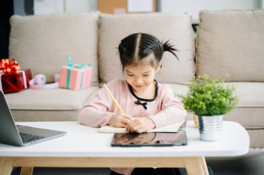 Evde öğrenen sevimli genç kız - masada dizüstü bilgisayarla resim çiziyor.