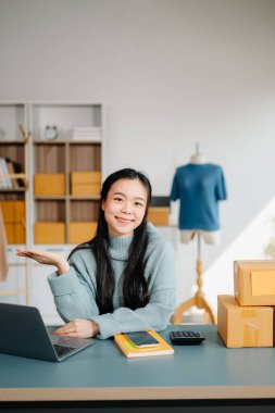 Genç iş kadını, bilgisayar ve el hareketleriyle modern bir ofisten online satış ve nakliyat yönetiyor.