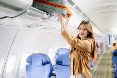 Asyalı bir kadın birinci sınıf bir uçakta bavulunu rafa koyuyor, lüks, rahat ve zarif bir seyahat sergiliyor. Havacılık, turizm ve iş hayatı teması için mükemmel.