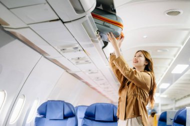 Asyalı bir kadın birinci sınıf bir uçakta bavulunu rafa koyuyor, lüks, rahat ve zarif bir seyahat sergiliyor. Havacılık, turizm ve iş hayatı teması için mükemmel.