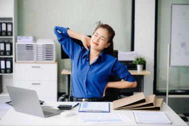 Ofis yorgunluğu çeken profesyonel bir kadın masasında sırt ağrısı çekiyor, işyerindeki sağlık durumunu ve sağlık sorunlarını vurguluyor.