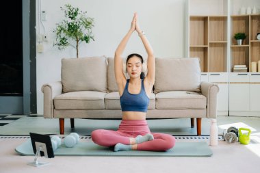 Asyalı kadın yoga yapıyor ve tabletten online dersler izliyor. Evde oturma odasında eğitim.