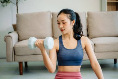 Paspas üzerinde dambıl kullanan genç bir Asyalı kadın, sağlığını, motivasyonunu ve modern ev ortamında sağlıklı bir yaşam tarzını sergiliyor..