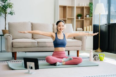 Asyalı kadın yoga yapıyor ve tabletten online dersler izliyor. Evde oturma odasında eğitim.