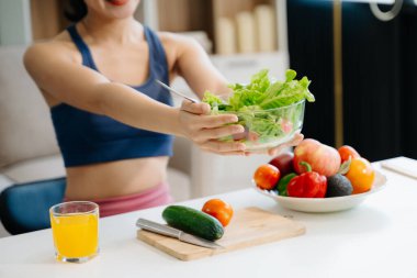 Formda bir Asyalı kadın evde taze salata, meyve suyu ve meyve suyu sever. Parlak, modern bir ev ortamında sağlığın, beslenmenin ve canlılığın vücut bulmuş hali. Sağlıklı bir yaşam tarzı!