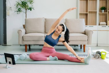 Asyalı kadın yoga yapıyor ve tabletten online dersler izliyor. Evde oturma odasında eğitim.