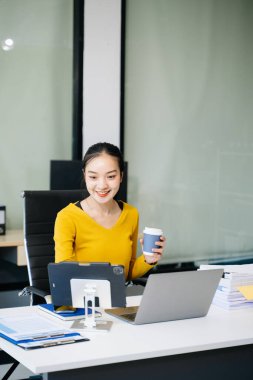 Modern ofis masasında kahve içerken tablet ve laptop kullanan başarılı Asyalı iş kadını. vergi, rapor, muhasebe, istatistik ve analitik araştırma kavramı
