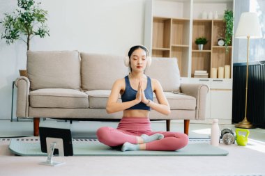 Asyalı kadın yoga yapıyor ve tabletten online dersler izliyor. Evde oturma odasında eğitim.