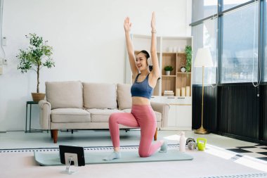 Asyalı kadın yoga yapıyor ve tabletten online dersler izliyor. Evde oturma odasında eğitim.