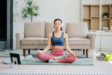 Asyalı kadın yoga yapıyor ve tabletten online dersler izliyor. Evde oturma odasında eğitim.