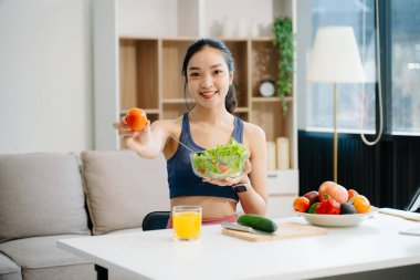 Formda bir Asyalı kadın evde taze salata, meyve suyu ve meyve suyu sever. Parlak, modern bir ev ortamında sağlığın, beslenmenin ve canlılığın vücut bulmuş hali. Sağlıklı bir yaşam tarzı!