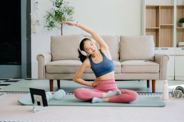 Asyalı kadın yoga yapıyor ve tabletten online dersler izliyor. Evde oturma odasında eğitim.