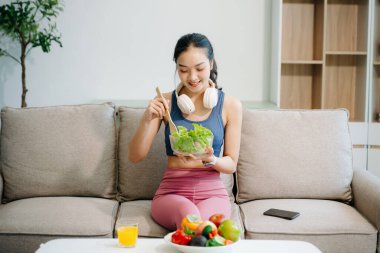 Formda bir Asyalı kadın evde taze salata, meyve suyu ve meyve suyu sever. Parlak, modern bir ev ortamında sağlığın, beslenmenin ve canlılığın vücut bulmuş hali. Sağlıklı bir yaşam tarzı!